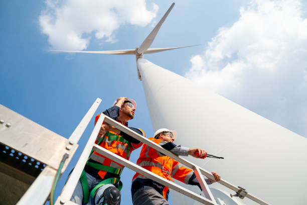 istock Two engineers or technician workers stand on base of big windmill or wind turbine and look to right side with blue sky. 1466437616