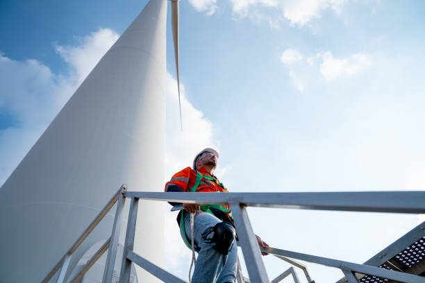 istock Caucasian engineer or technician worker walk down at base of windmill or wind turbine and look forward with blue sky and day light. 1466437671