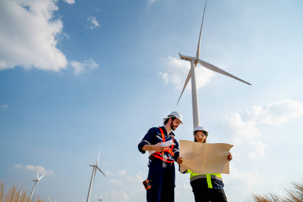 istock Lower view of Caucasian engineer or technician man and woman discuss together using drawing paper and stay in front of row of windmill or wind turbine with blue sky. 1466437680