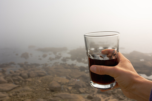 A woman's hand with a glass glass in nature, Fog in the distance ocean and shore of stones, atmospheric and fresh. The background is beautiful and there is a place to sign