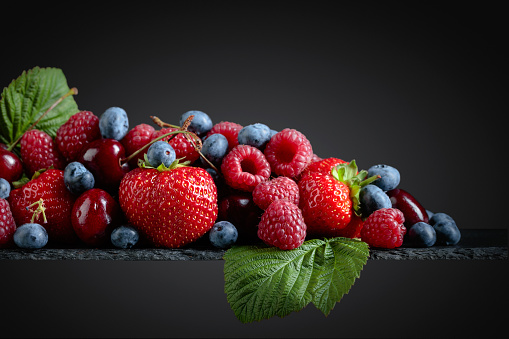 Berries closeup colorful assorted mix of strawberry, blueberry, raspberry and sweet cherry in studio on dark background.