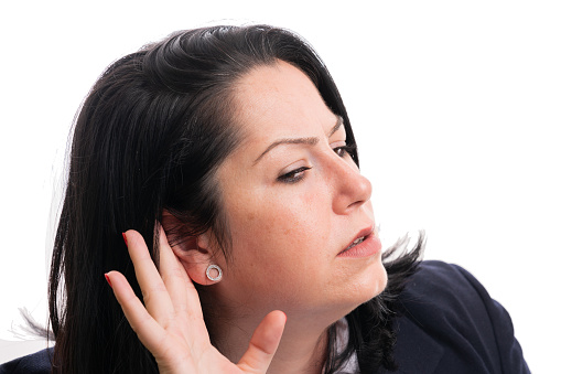 Close-up of curious adult businesswoman touching ear with index finger hand as listening corporate secret concept isolated on white studio background