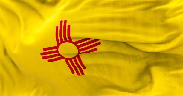 Detail of the New Mexico state flag waving. Red sun, symbol of the Zia people, displayed on a yellow background. 3d illustration render. Selective focus. Close-up. Textured background
