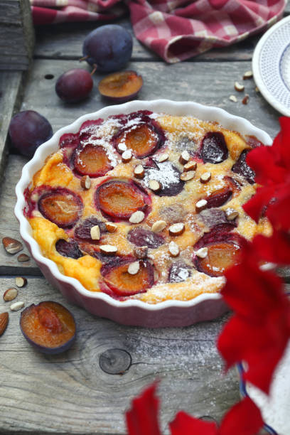 Damson blue plum clafoutis (flan), icing sugar and almonds dressing, french cuisine on wooden background. Rustic style. Top view