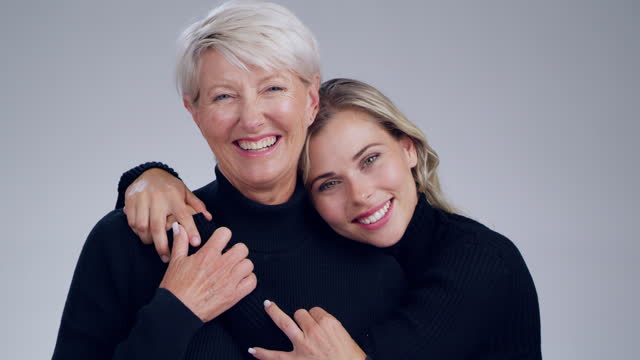 Face, family or fashion with a mother and daughter in studio on a gray background together for style. Portrait, beauty or smile with a happy senior woman and adult child indoor to promote clothes
