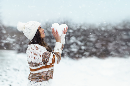 Woman holds snow heart in winter landscape
