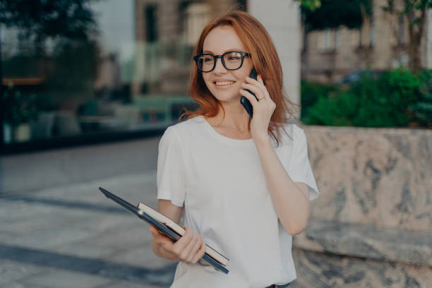 istock Happy ginger woman has telephone conversation looks into distance holds tablet and notebook 1466463183