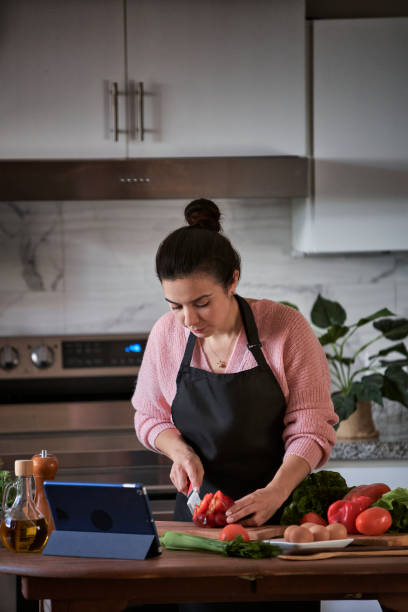 istock Hispanic young woman taking online training classes to prepare recipe at the kitchen 1466463432