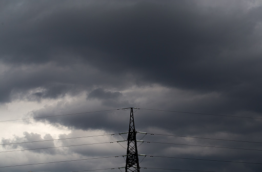 Electricity transmission pylon silhouetted against a cloudy sky.