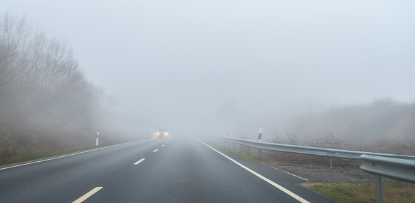 Car drives on a road in the fog. The headlights shine brightly.