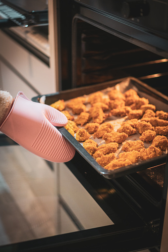 Women hand cooks Chicken nuggets in the oven