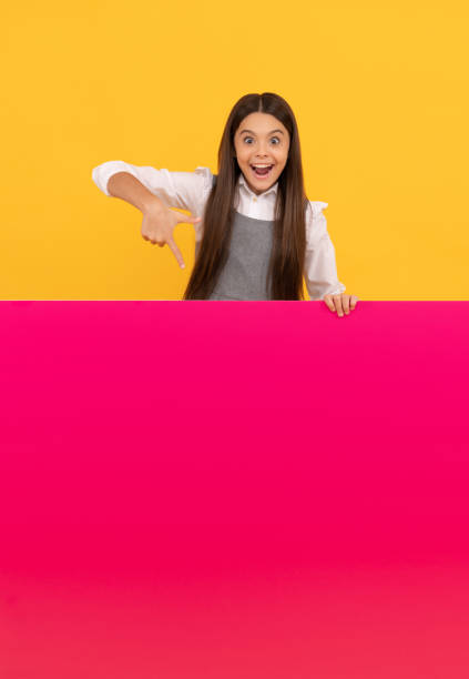 amazed kid pointing finger on blank pink paper sheet for copy space, advertisement.