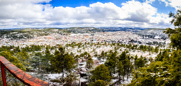 Panorámica de pueblo en invierno visto desde las alturas, nieve cubriendo las montañas, bosque blanco, cielo azul con nubes, sierra tarahumara en creel Chihuahua
