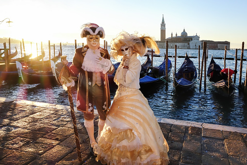 Venice, Italy - March 01, 2022: Couple dressed in traditional costumes stand in front of the Ducal palace, part of the Venice Mask Carnival, Veneto, Italy