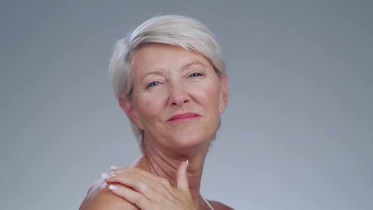 Senior woman, face and laughing in skincare, cosmetics or makeup against a gray studio background. Portrait of elderly female model with smile and laugh in satisfaction for facial beauty on mockup