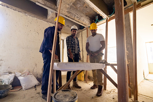 Group of Latin American construction workers looking at blueprints at a building site