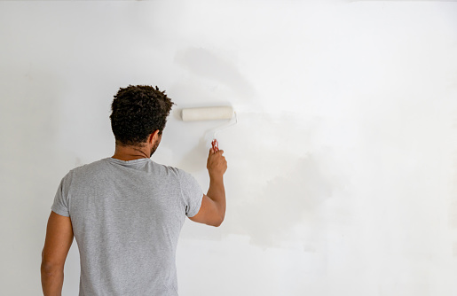 Rear view of an African American man painting a wall in his house using a paint roller