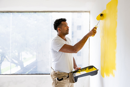 Latin American house painter painting a wall with yellow paint using a roller - home improvement concepts