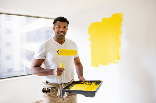 Latin American house painter painting a wall yellow using a paint roller - home improvement concepts