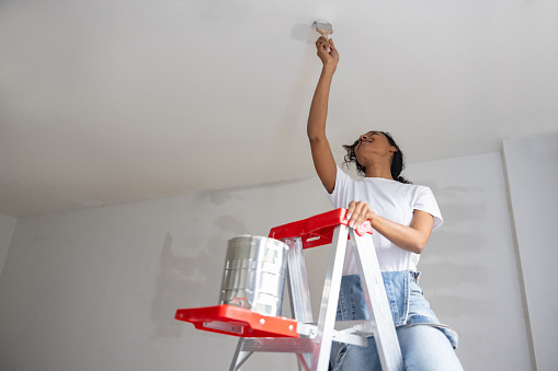 Happy African American woman painting the ceiling of her house using a ladder - home improvement concepts