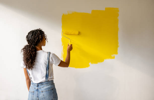 istock Woman painting a wall yellow while remodeling her house 1466480249