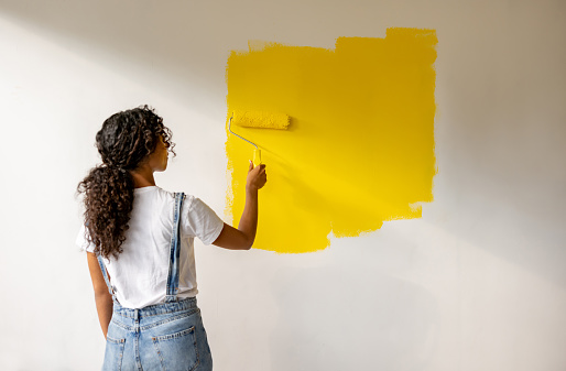 Rear view of an African American woman painting a wall yellow using a paint roller - home improvement concepts