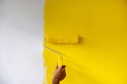 Close-up on a woman painting a wall yellow using a paint roller - interior design concepts