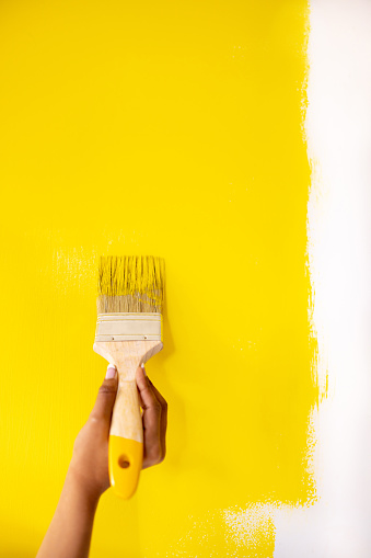 Close-up on a woman painting a wall with yellow paint using a brush - interior design concepts