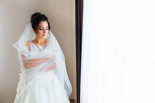 beautiful bride in wedding dress and bridal veil embraces herself. bride standing at the window