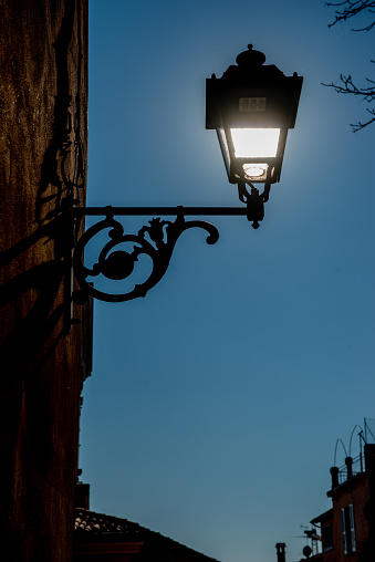 Old wrought iron lamppost lit with the cathedral of Brescia in the background