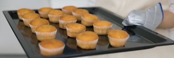istock Hand of baker wearing mitten, holding tray with muffins 1466487809