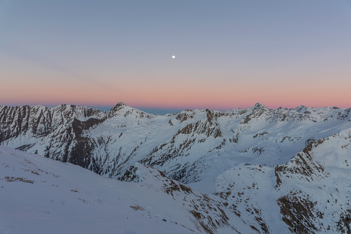 The moon over the snowy mountains illuminated by the last lights of the day Val Brembana Italy Europe