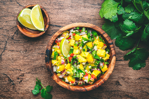 Spicy mango salsa sauce with red chili peppers, onion, garlic lime and cilantro, rustic wooden table background, top view