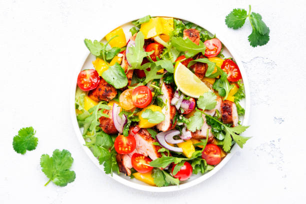 istock Fresh salad with grilled chicken slice with mango salsa, tomato, cilantro, red onion and lettuce in mexican style, white table background, top view 1466489504
