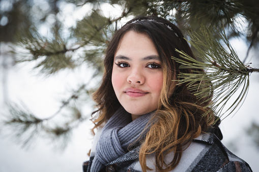 Beautiful hispanic teenage girl smiling in the woods. Winter in Colorado. Snowy forest. Senior photos. High school senior.