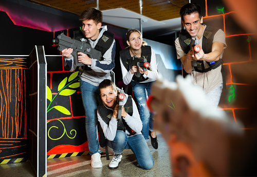 Excited young people playing enthusiastically laser tag game two teams opposite each other in dark room