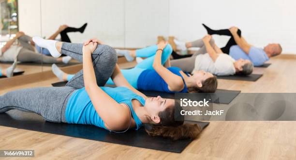 People Of Different Ages Stretching Their Glutes While Lying On Mats During Pilates Workout In Gym Stock Photo - Download Image Now