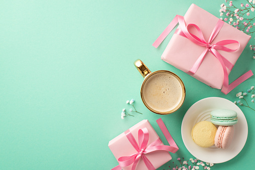 Spring concept. Top view photo of pink gift boxes with ribbon bows plate with macarons cup of fresh coffee and gypsophila flowers on isolated turquoise background with copyspace