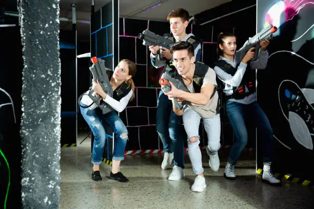 Photo of Modern young people with laser pistols playing laser tag on dark labyrinth