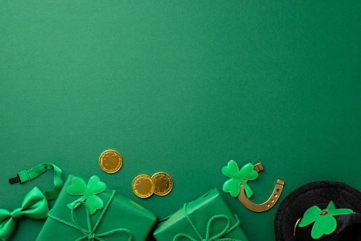 St Patrick's Day concept. Top view photo of gift boxes leprechaun hat bow-tie gold coins horseshoe and trefoils on isolated green background with empty space