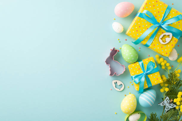 istock Easter concept. Top view photo of yellow gift boxes with blue bows easter eggs bunny shaped baking mold mimosa flowers butterfly and sprinkles on isolated pastel blue background with copyspace 1466503181
