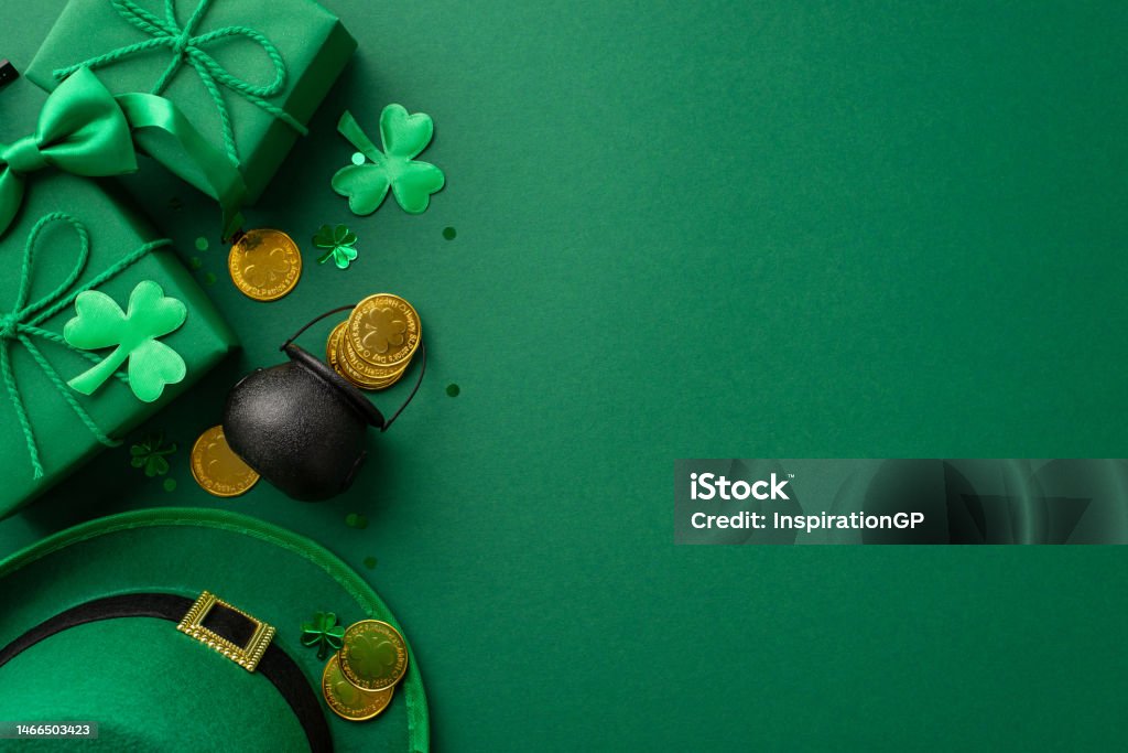 St Patrick's Day concept. Top view photo of leprechaun headwear gift boxes pot with gold coins bow-tie clovers and confetti on isolated green background with empty space St. Patrick's Day Stock Photo