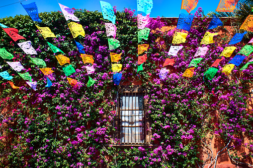 Fachada de casa con flores, calle adornada con papel mache de colores, formas y figuras, casa de san Miguel de allende guanajuato