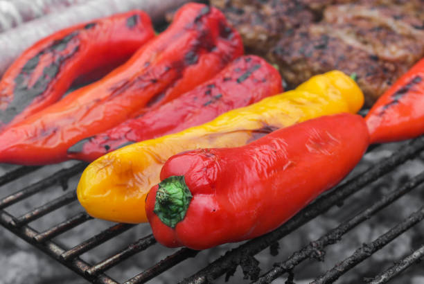 Seasonal red and yellow peppers fried on a grill with meat in the backyard of the house, close-up side view. Grill food concept.