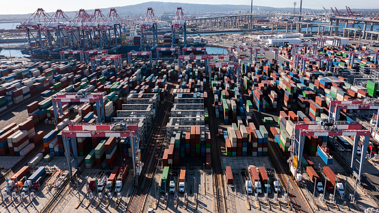 Daytime aerial view of an intermodal container shipping stock yard unloading vessels at port.