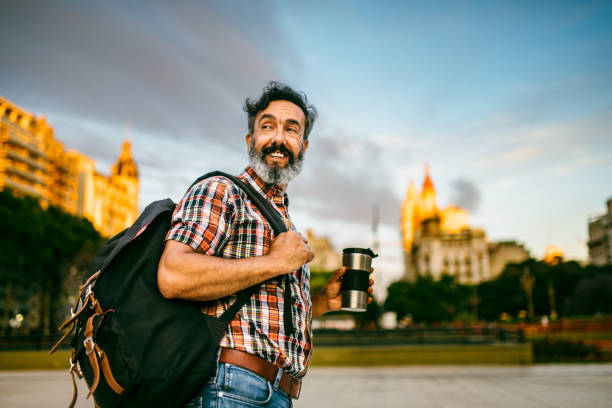 Mature commuter walking to work with a backpack and a travel mug at sunrise