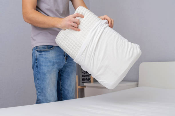 istock Man tucks an orthopedic pillow with a fresh bright white pillowcase. Making the bed with fresh bed linen by white man. The day of change of bed linen. The day of washing bed linen in the laundry room. 1466526990