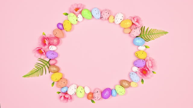 Easter round copy space frame. Painting brush leaving behind eggs and spring flowers on pastel pink background. Stop motion. Flat lay