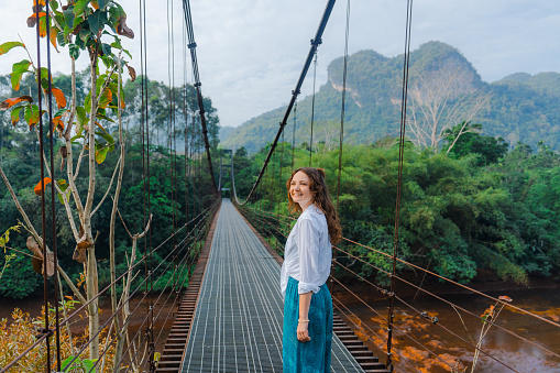 Young Caucasian woman in elegant clothing walking on suspension bridge in the jungles