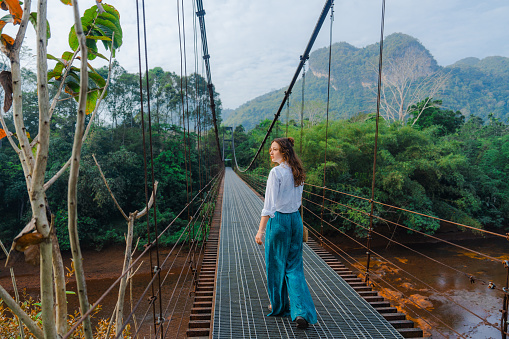 Young Caucasian woman in elegant clothing walking on suspension bridge in the jungles